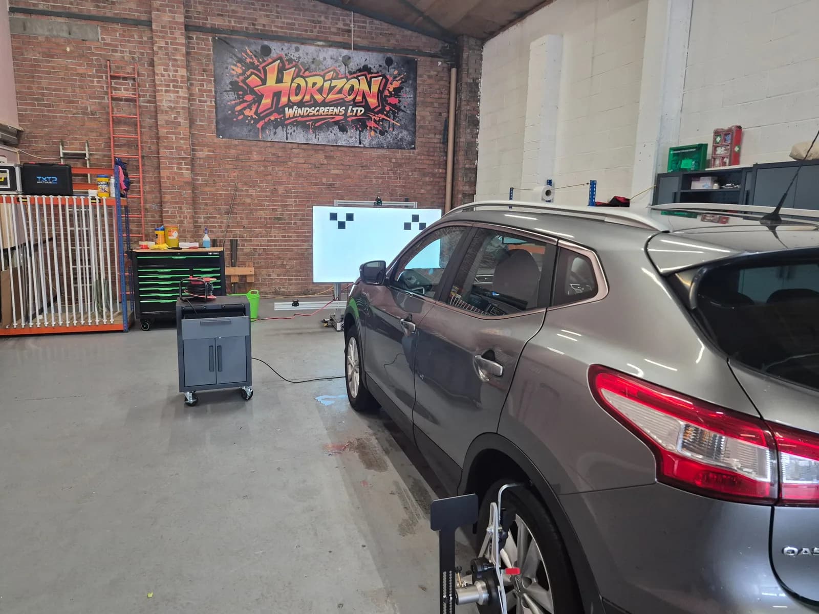 Vehicle positioned with wheel-mounted equipment facing an ADAS calibration target inside Horizon Windscreens' workshop.