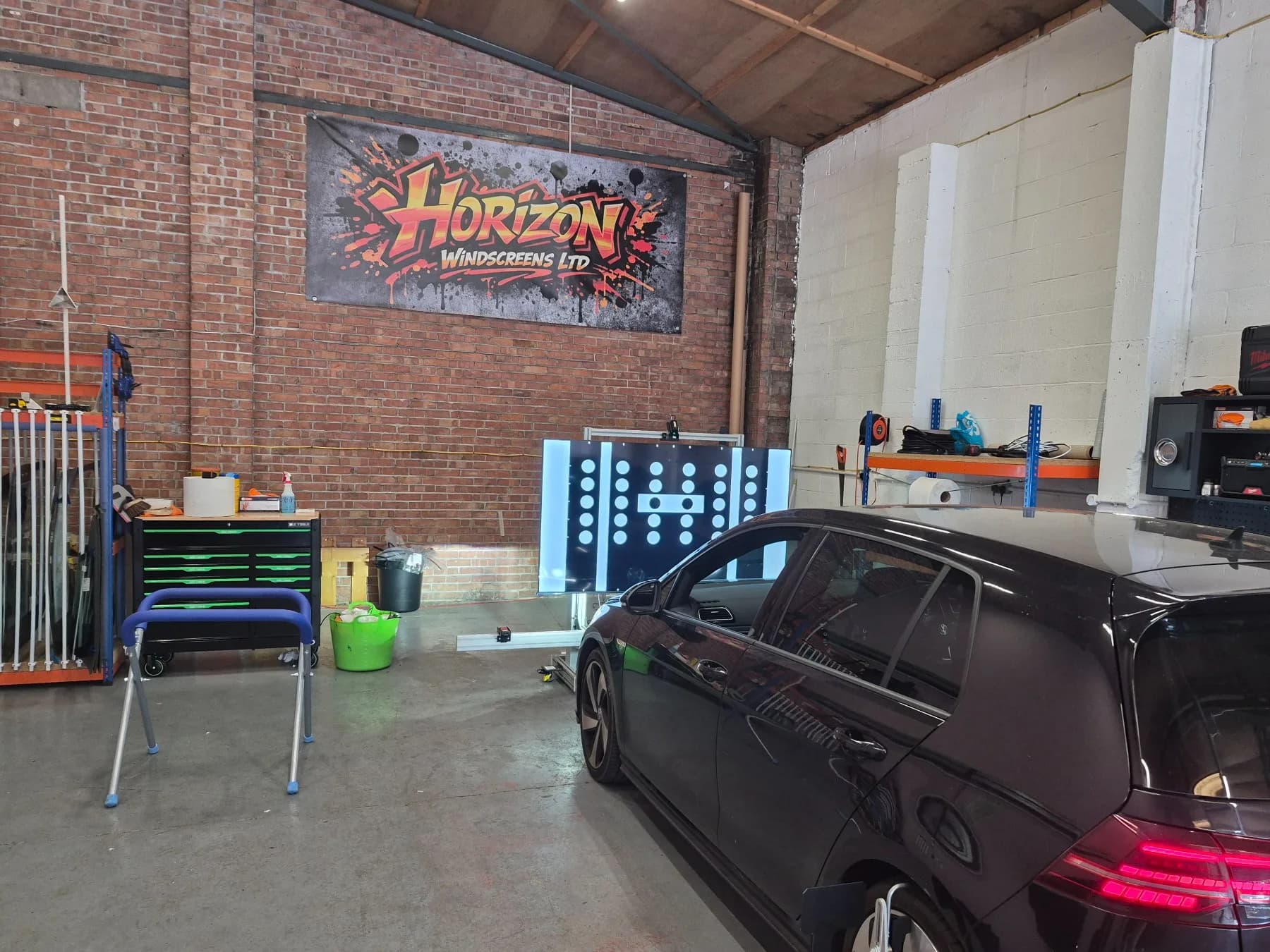 Vehicle positioned beside an illuminated ADAS calibration target in the Horizon workshop.