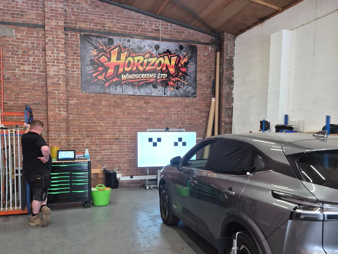 Grey vehicle positioned beside an ADAS calibration target in the Horizon workshop.