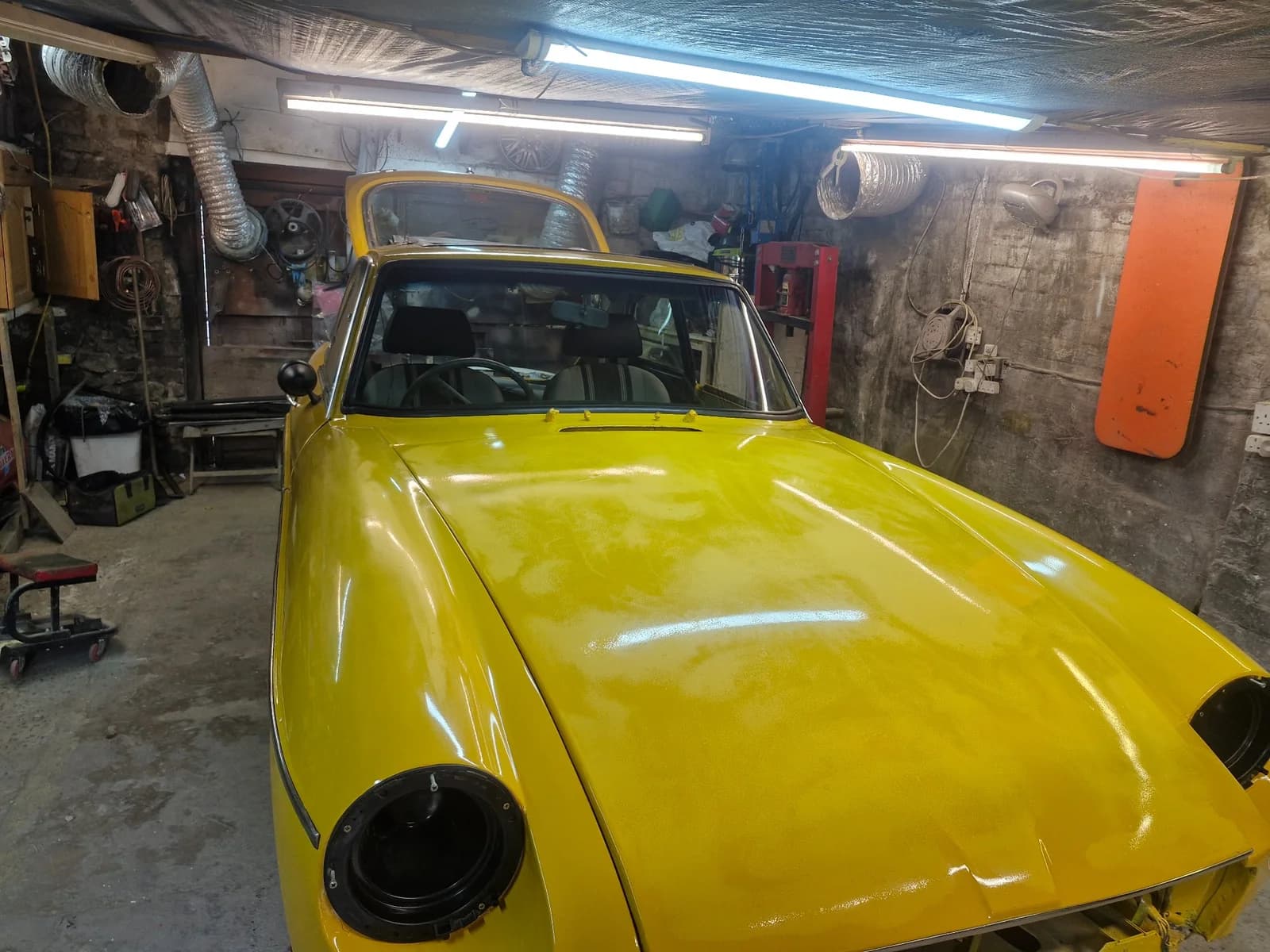 Yellow classic vehicle inside a working vehicle workshop.