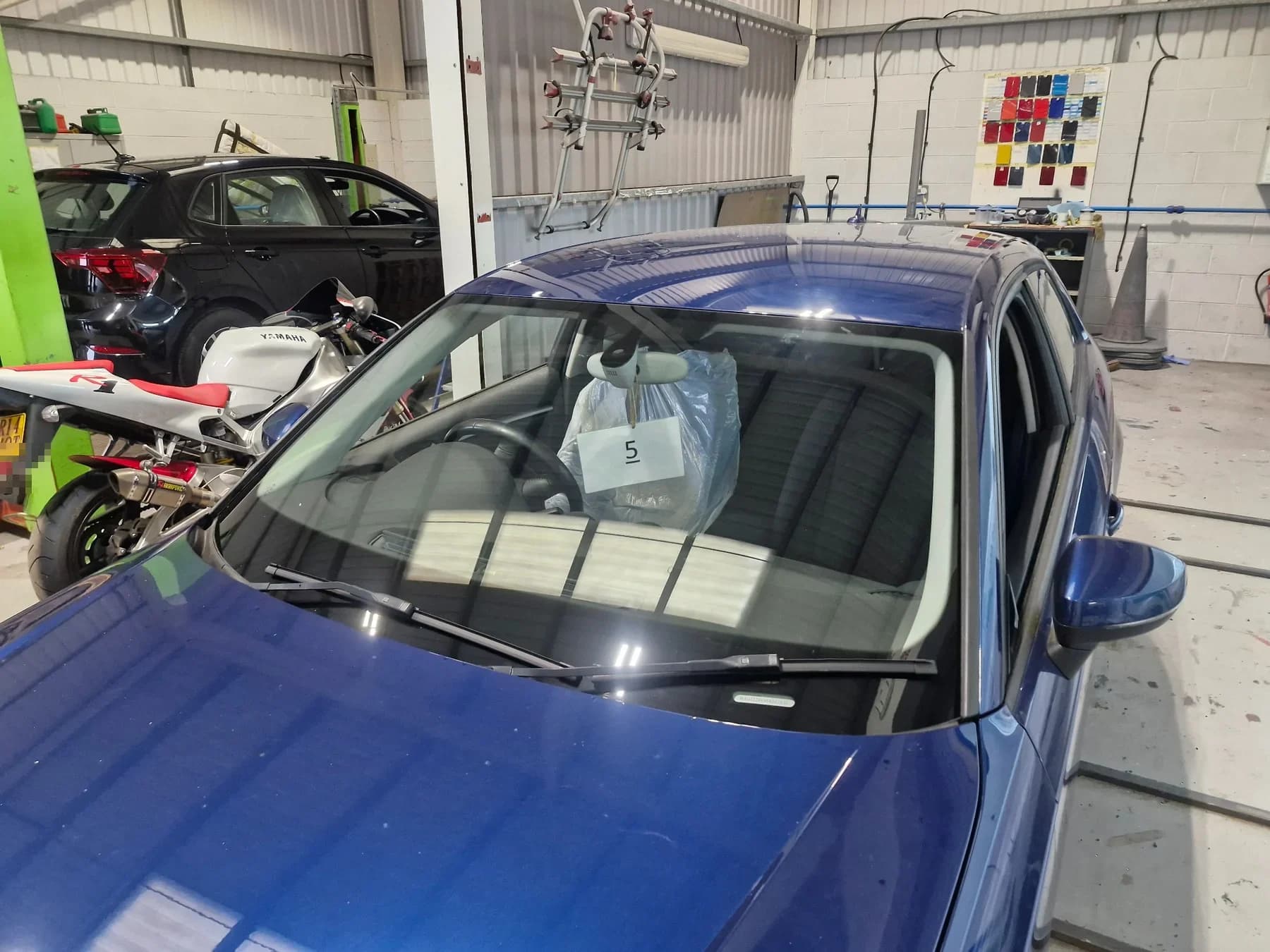 Blue vehicle with its windscreen visible inside the workshop.